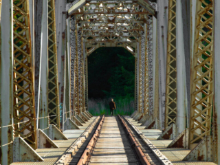An abandoned train bridge with a person walking along the tracks in the distance.