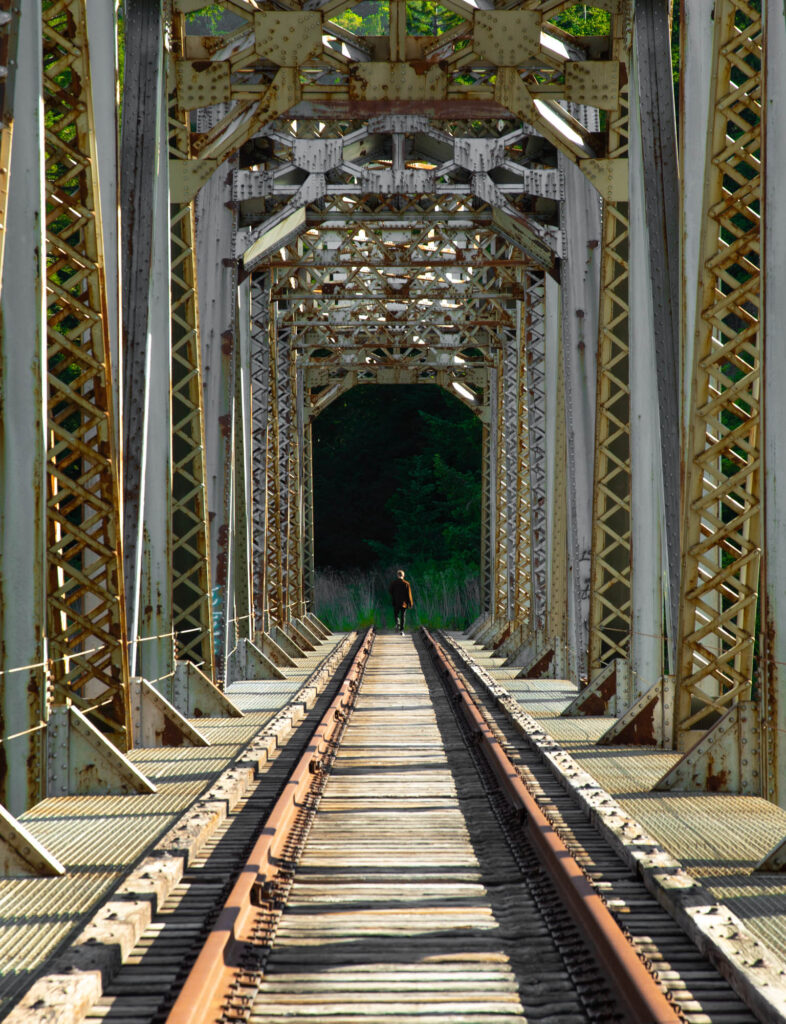 An abandoned train bridge with a person walking along the tracks in the distance.