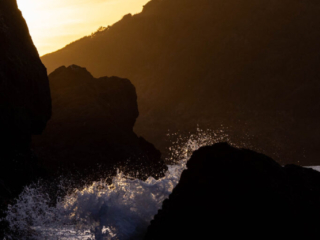 The ocean splashes over some rocks at sunset