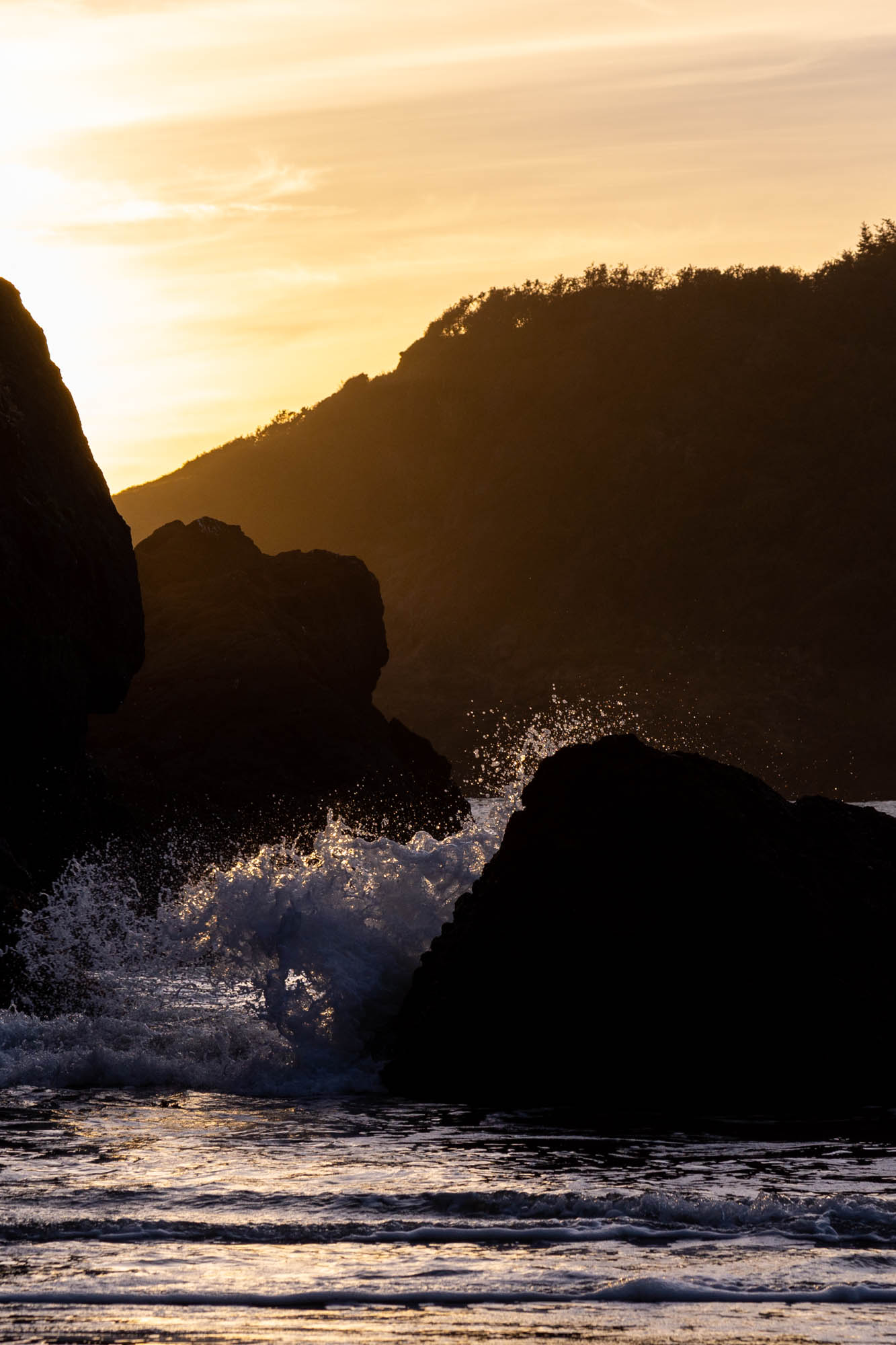 The ocean splashes over some rocks at sunset