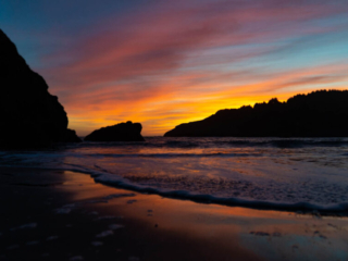 The edge of the ocean rolls in on a rocky coastline under a cloudy sunset