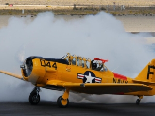 An airplane taxies across the tarmac and blows smoke in celebration. A person leans out of the back window and waves an orange flag.