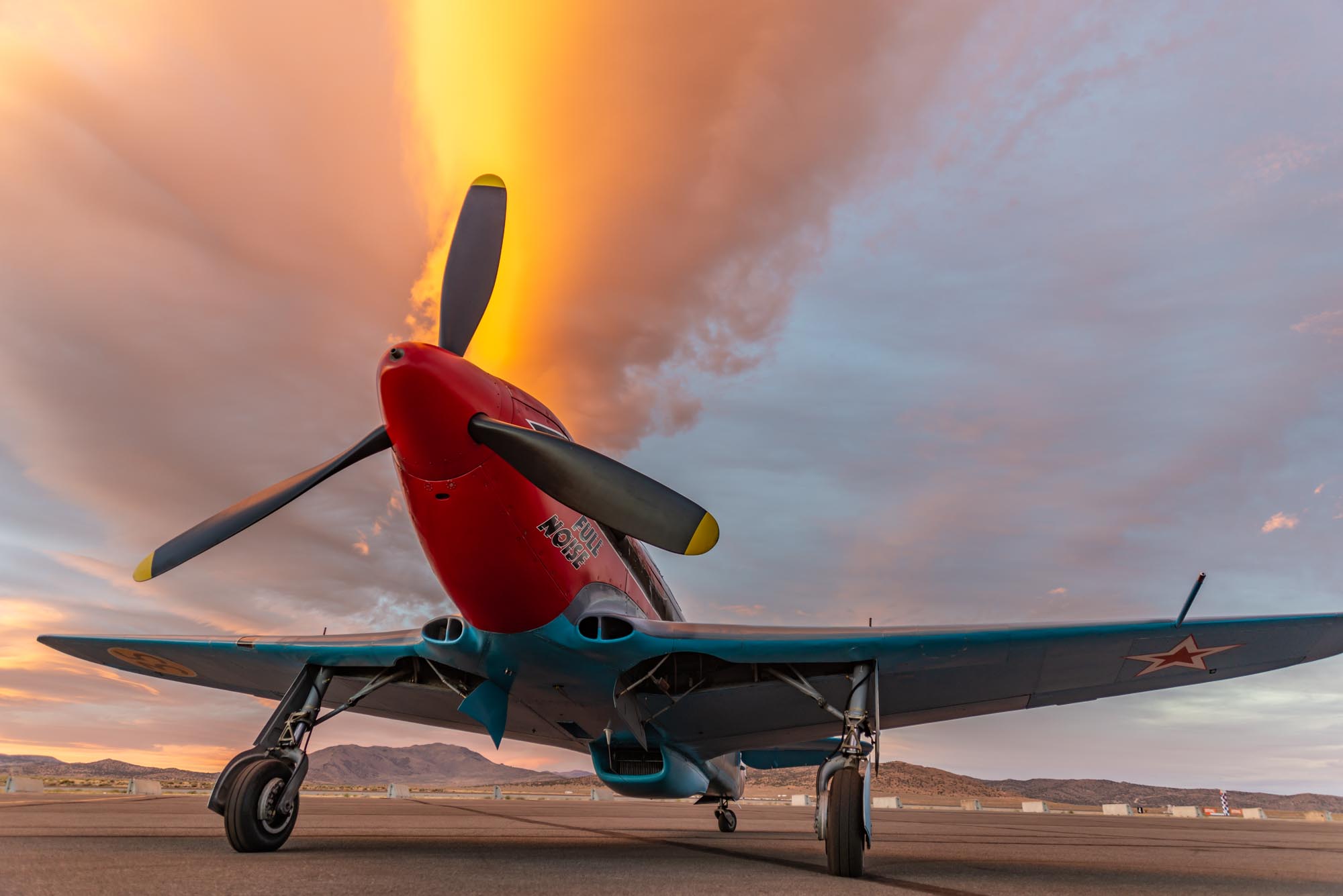 An airplane sits parked on the tarmac with a dramatic sky in the background