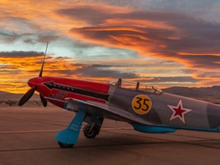 An airplane sits parked on the tarmac with a dramatic sky in the background