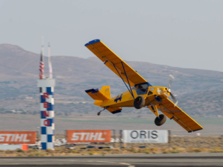 A STOL race plane flies past the home pylon, flying at a dramatic angle.