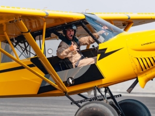 A smiling man taxis by in an airplane and gives a shaka sign