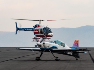 An airplane taxis across the ramp while a helicopter hovers in the background.