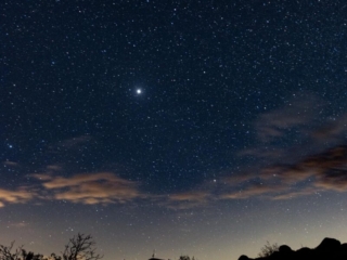 A number of stars sit behind some clouds and rocks.