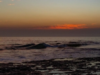 Several waves ripple across the frame in front of the sunset.