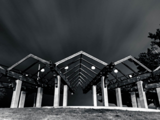 A black and white photo of an amphitheater at night. Clouds roll overhead in dramatic streaks