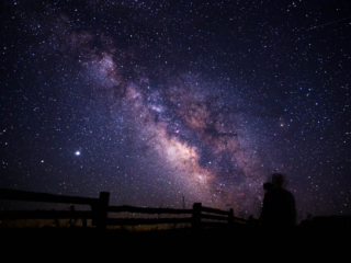 A view of the milky way, with a fence and a person in the foreground