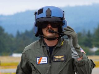 A man wears a flight suit and a pilot-style helmet and looks at the camera