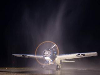 A parked airplane runs its engine late at night, while water is sprayed over the top of it