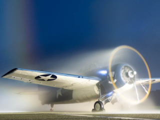 A parked airplane runs its engine late at night, while water is sprayed over the top of it