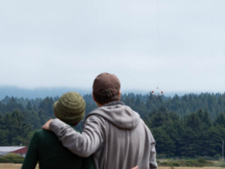 A Coast Guard helicopter hovers, while a couple stands in the foreground hugging each other